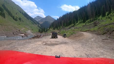 pov over red vehicle hood on narrow off road trail trail while driving past dirt bikes and ohv