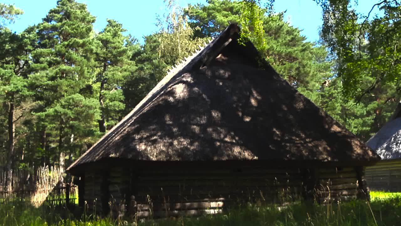 Old log cabin or a traditional farm house with a thatched straw roof during a summer or autumn sunny day at an open air museum in Tallinn. The medieval building has a wooden fence around grassy garden