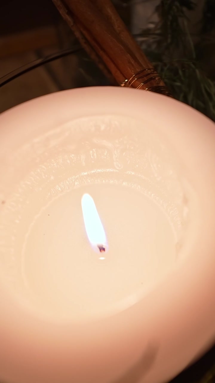 Golden-hour close-up of a lit white candle in a glass bowl with rosemary and cinnamon, creating cozy spa-like aromatherapy mood for winter home decor.