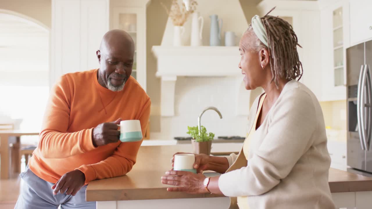 Lykkelig afroamerikansk seniorpar drikker kaffe på kjøkkenet, sakte film