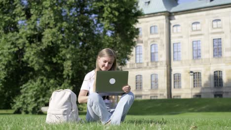 woman on grass using laptop outdoors near a plant window and building