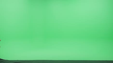 green screen studio: beautiful young woman wearing backpack and headphones using smartphone listens to the music or podcast dances happily across chroma key room