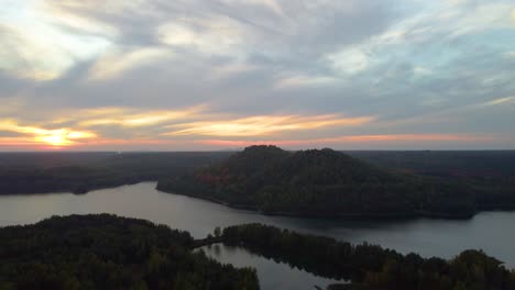 Terreno-Montañoso-Cubierto-De-Bosque-Otoñal-Cerca-Del-Agua-Del-Lago-Durante-La-Puesta-De-Sol-Dorada