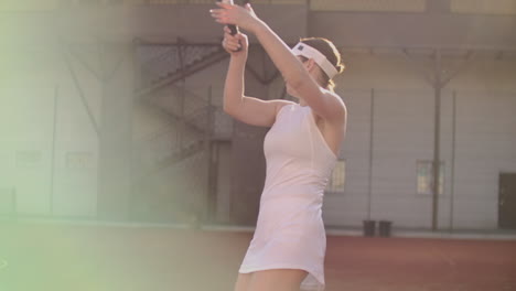 Cheerful-athlete-waiting-for-tennis-ball.-Skillful-female-tennis-player-is-preparing-to-beat-a-ball.-She-is-holding-a-racket-and-posing.-Woman-is-standing-on-tennis