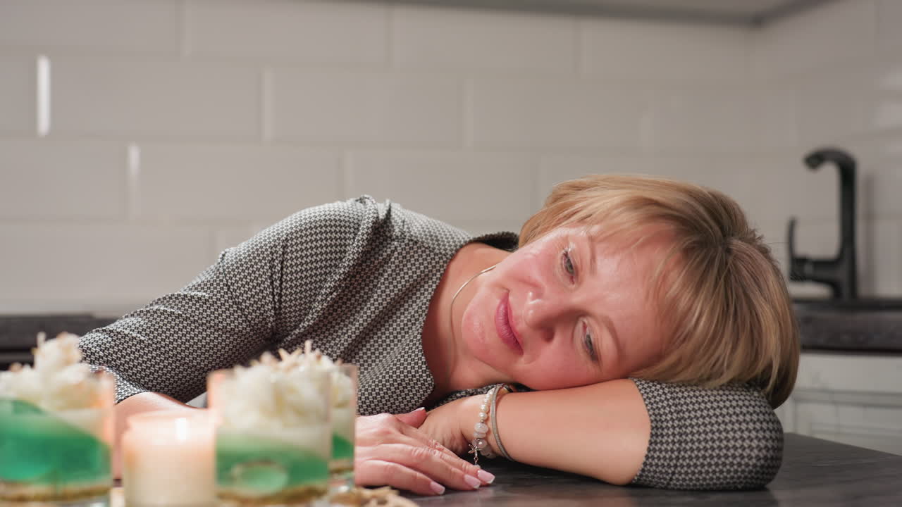 Round view of mother resting on table with gentle smile and calm presence in cozy kitchen space, expressing quiet admiration and relaxation after a fulfilling task with natural sunlight reflection