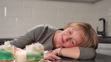 round view of mother resting on table with gentle smile and calm presence in cozy kitchen space, expressing quiet admiration and relaxation after a fulfilling task with natural sunlight reflection