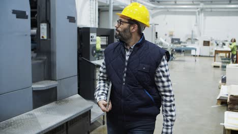 serious technician walking with laptop at factory