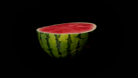 static close up of illuminated rotating half watermelon in studio with black background