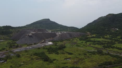 Aerial-view-of-a-mountain-of-debris-or-a-rubble-heap-with-dumper-trucks-unloading-more-rock-debris-from-a-tunnelling-project-in-a-hilly-region-impacting-the-local-ecology-and-terrain