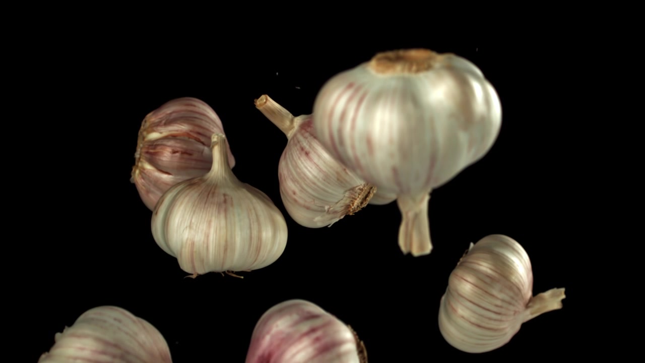 Bulbi d'aglio freschi che galleggiano verso l'alto su sfondo nero