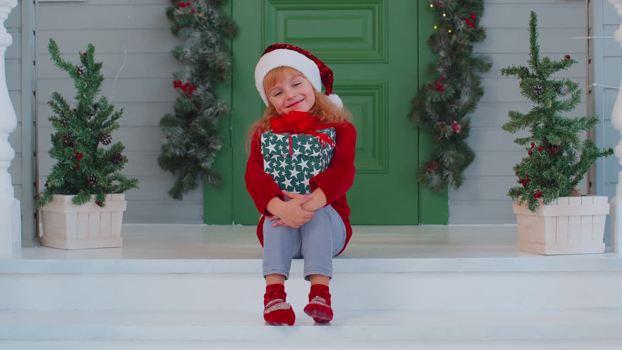 alegre niño sonriente niño niña niño sentado en el porche de la casa decorada sosteniendo una caja de navidad