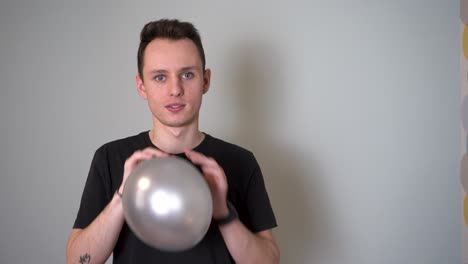 Young-Man-Blowing-a-Purple-Balloon-Against-Grey-Background