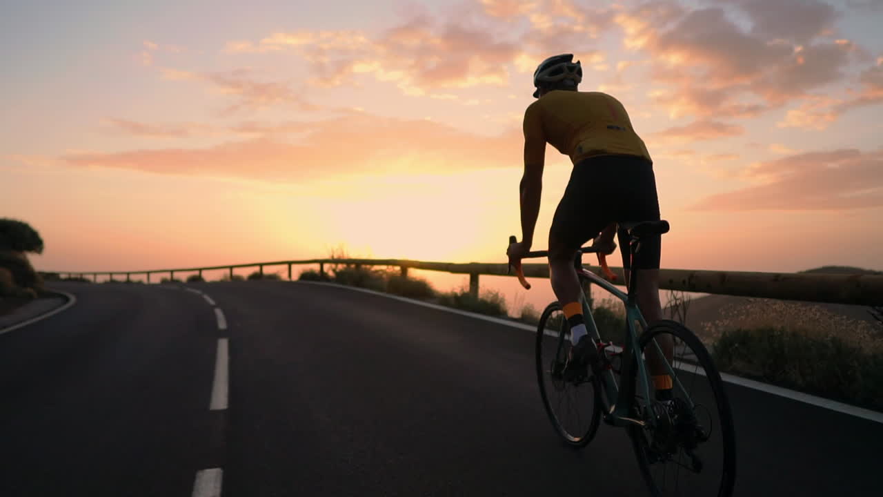 Slow motion captures the athlete cycling on a mountain serpentine, savoring the island's view, symbolizing a commitment to a healthy lifestyle during sunset