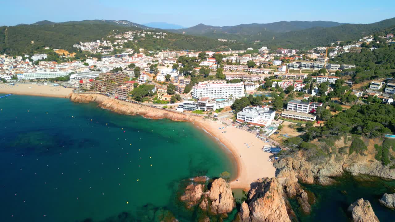 Picturesque costa brava aerial views showcasing the stunning turquoise waters, beautiful sandy beach, lush green hills, and rocky coastline under a clear blue sky