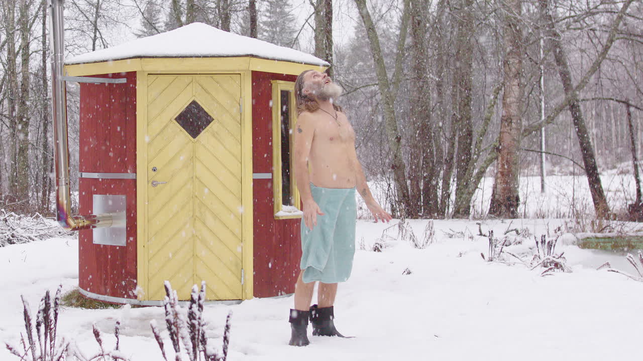 Wild man in snow near sauna looks up at heavens as snow falls, talks to God
