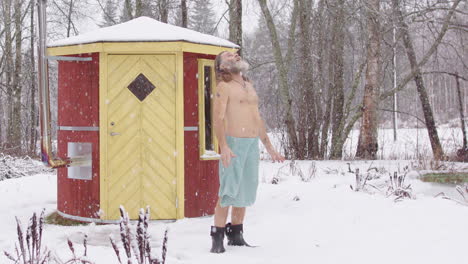 wild man in snow near sauna looks up at heavens as snow falls, talks to god
