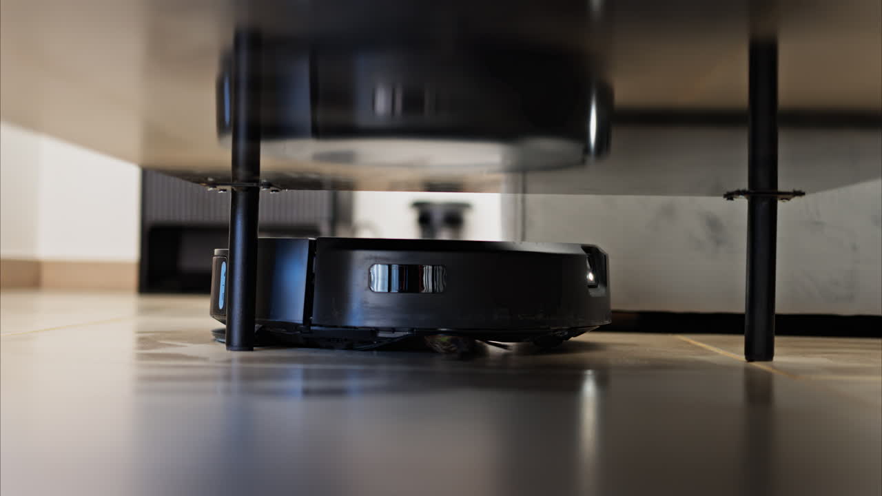 Close up of a small, black robot vacuum cleaning under surfaces in the house