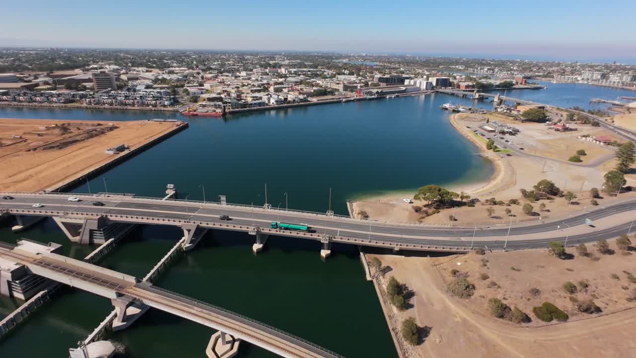 drone view from high showing port adelaide and a bridge with cars running over it, it is a sunny day and the vegetation is dry