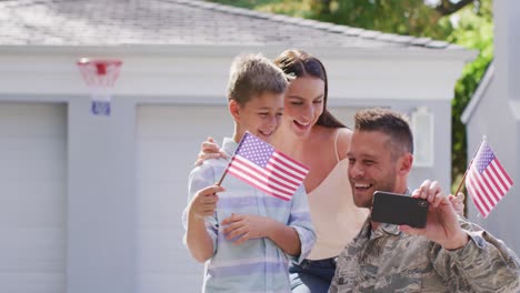 Glücklicher-Kaukasischer-Männlicher-Soldat,-Der-Ein-Selfie-Mit-Seinem-Lächelnden-Sohn-Und-Seiner-Frau-Im-Garten-Vor-Ihrem-Haus-Macht