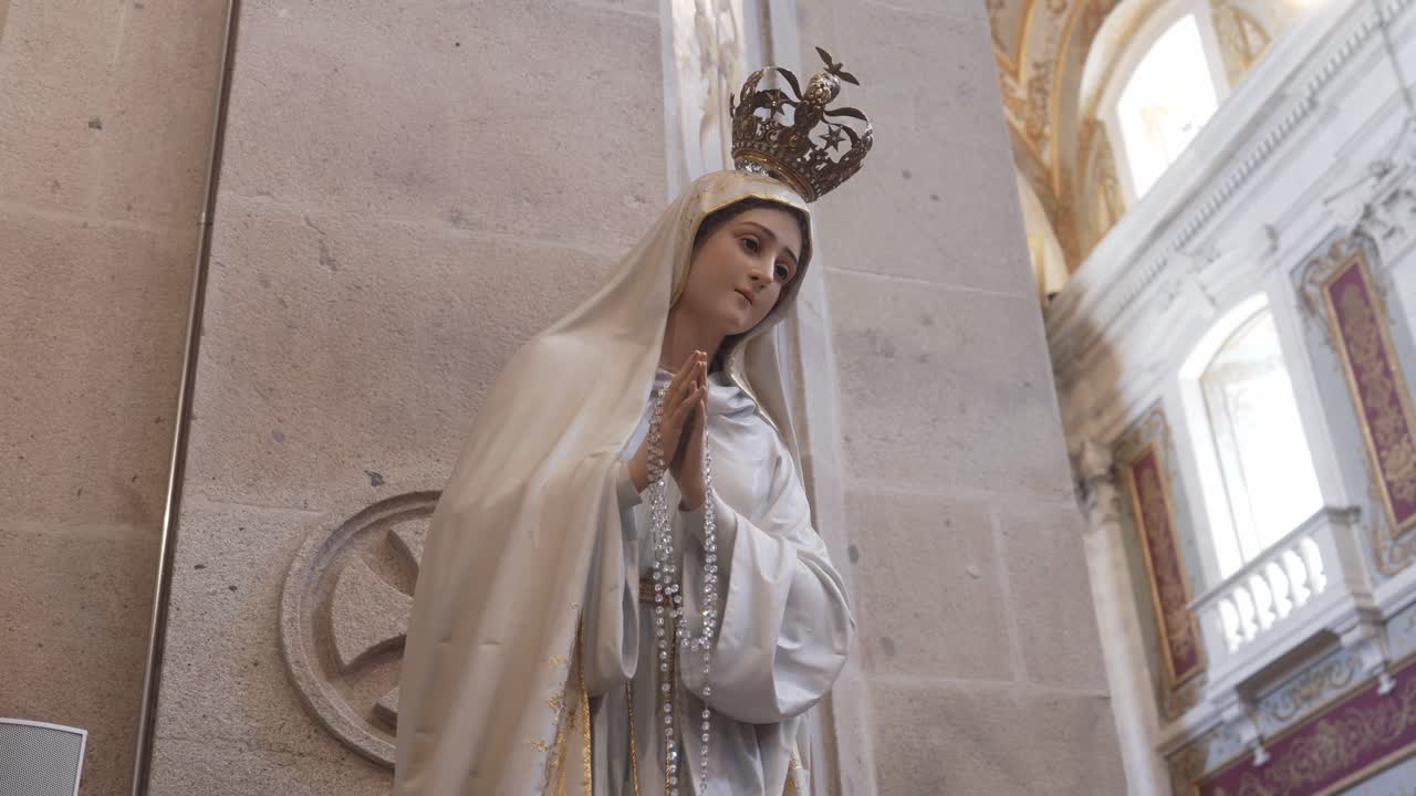 Statua della Vergine Maria con corona e rosario all'interno di una chiesa.