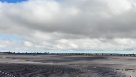 camera slowly pans across expansive solar panel array, overcast daylight, rural australian landscape visible