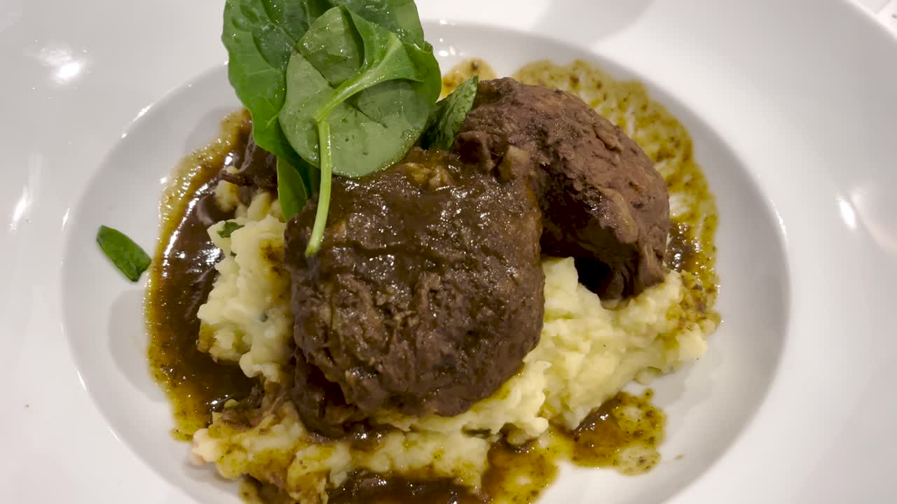 A beautifully plated dish featuring a rich, dark piece of meat, likely braised or slow-cooked, resting on a bed of creamy mashed potatoes.