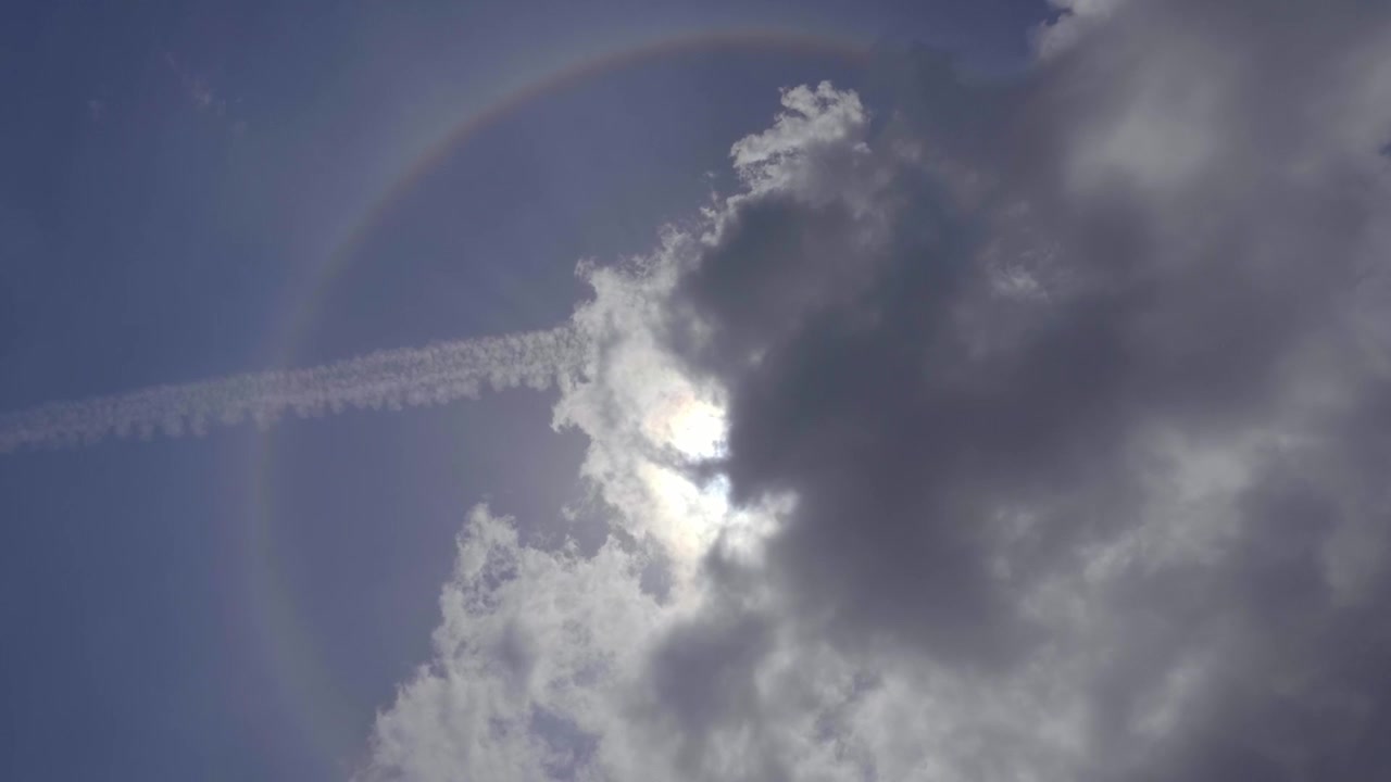 Kreisförmiger Regenbogen am Himmel mit der Sonne hinter den Wolken.