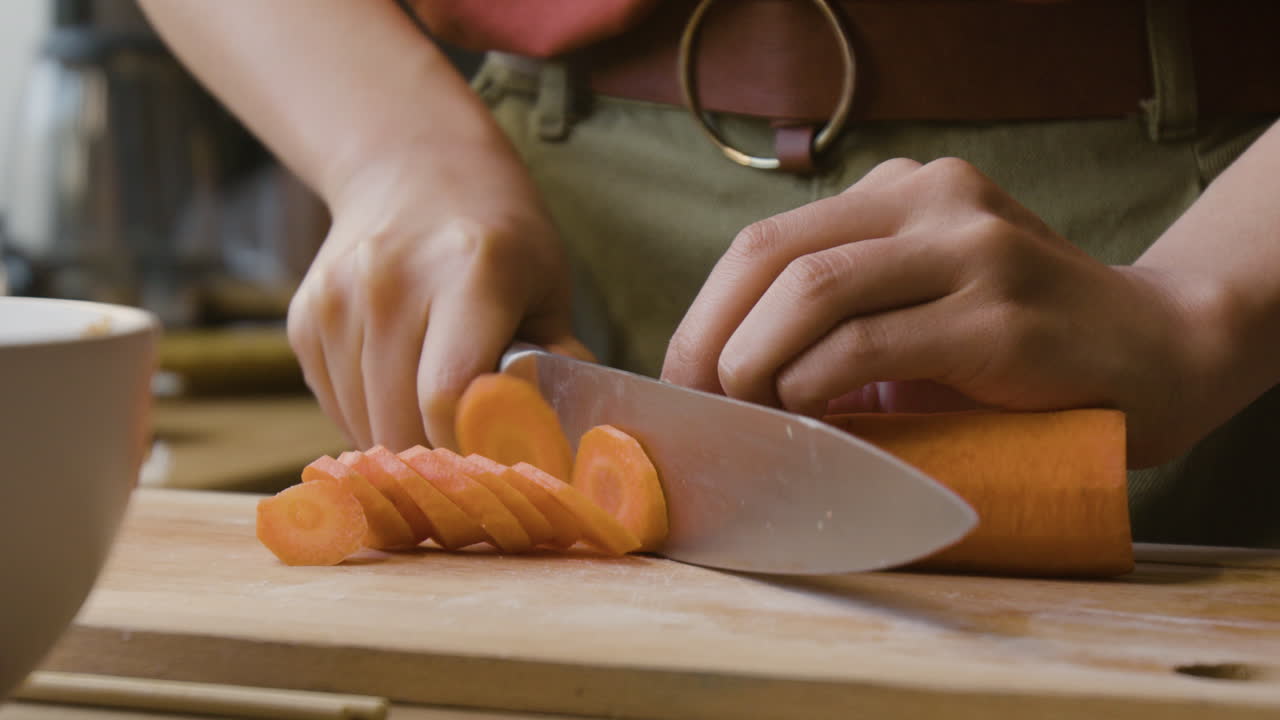 Close-up of hands slicing carrots on a cutting board