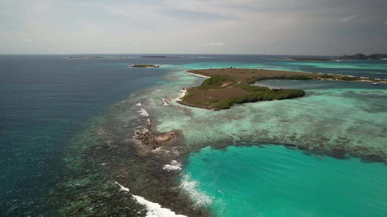 Acque costiere turchesi con litorali sabbiosi e piccole isole sotto un cielo nuvoloso, vista aerea.