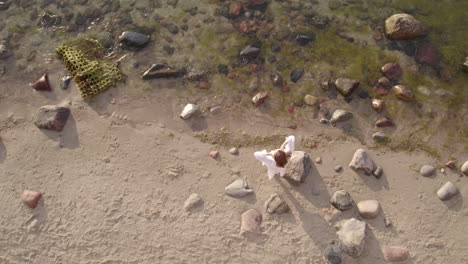 graceful beautiful woman in white dress enjoys sunlit lonely rocky beach