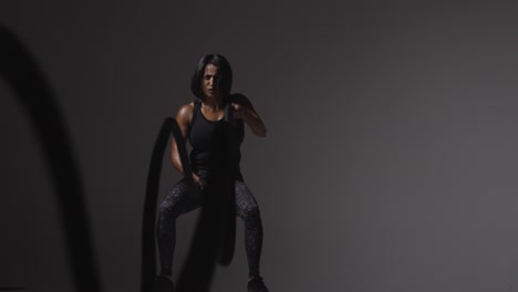 studio shot of mature woman wearing gym fitness clothing doing cardio exercise with battle ropes 2