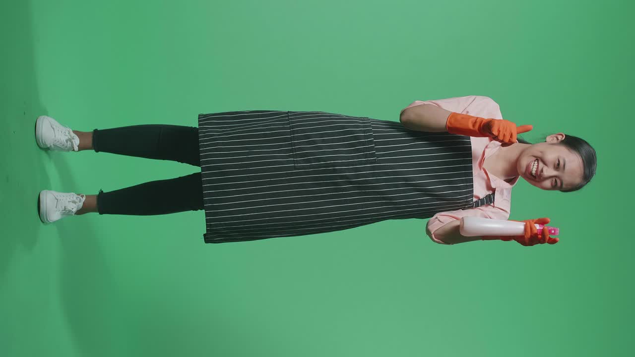 손에 스프레이를 보고 그린 스크린 스튜디오에서 카메라에 엄지손가락을 보여주고 있는 아시아 여성 집주인의 몸집이 가득 차 있습니다.