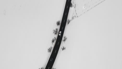 aerial shot of car driving on road in natural winter landscape, snow covered country