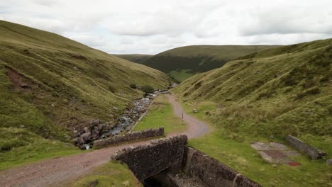 Brecon-beacons-countryside-valley-footpath-Llyn-y-fan-Fach-mountain-range-low-aerial-view-along-green-mountain-wilderness