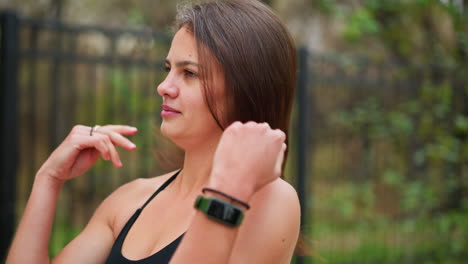 close-up portrait of woman packing her hair while standing outdoors, woman tying back hair, preparing for exercise or workout, with a background of green foliage and iron fence