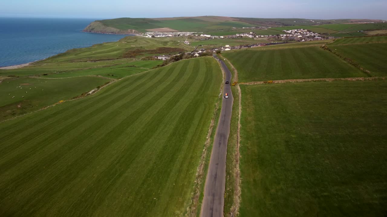 Aerial shot of two cars driving along the coast of United Kingdom