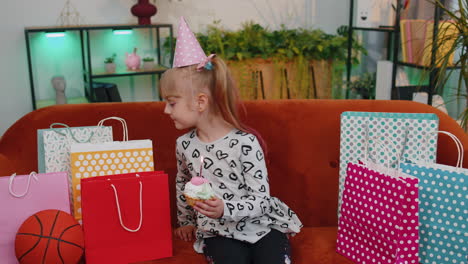 happy child girl with lots of gifts celebrating birthday party making a wish, blowing cake candle