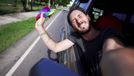 Zeitlupe-Eines-Kaukasischen-Männlichen-Schwulen,-Der-Den-Lesbischen-LGBT-Stolz-Feiert-Und-Vor-Dem-Fenster-Des-Autos-Eine-Regenbogenfahne-Weht,-Während-Er-Schnell-Auf-Der-Autobahn-Fährt