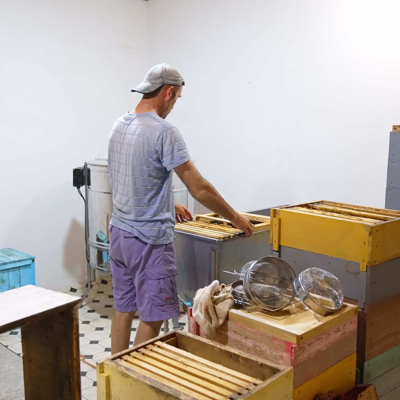 Light room with wooden hives and boxes in it. Male apiculturist replaces honey frames from one box to another