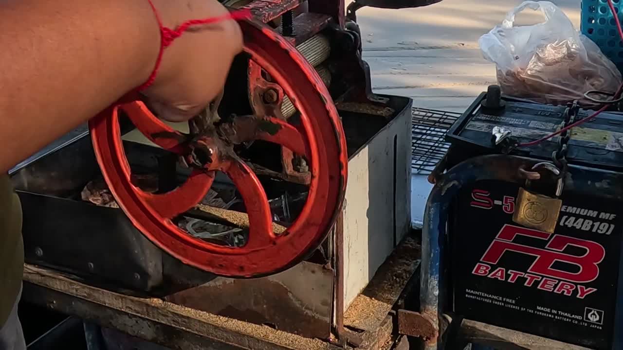 A person manually turns a red mechanical wheel next to a battery on a seaside platform.