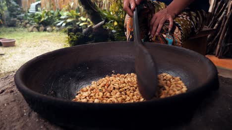 Medium-slow-motion-shot-of-roasted-coffee-beans-kopi-luwak-while-the-beans-are-stirred-and-roasted-in-a-wok-with-a-wooden-spoon-by-one-of-the-coffee-plantation's-employees-in-Bali-indonesia