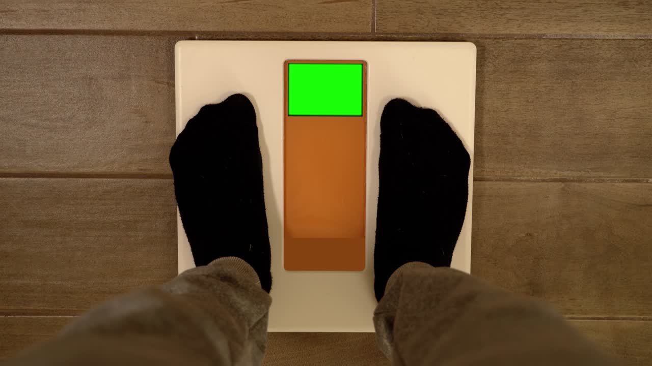 Man in sportswear steps on scales with green screen at home