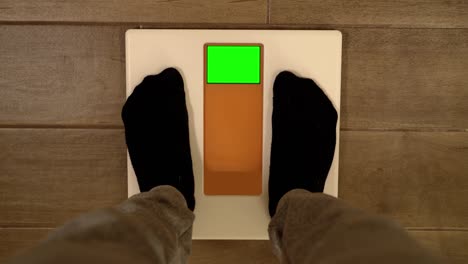 man in sportswear steps on scales with green screen at home