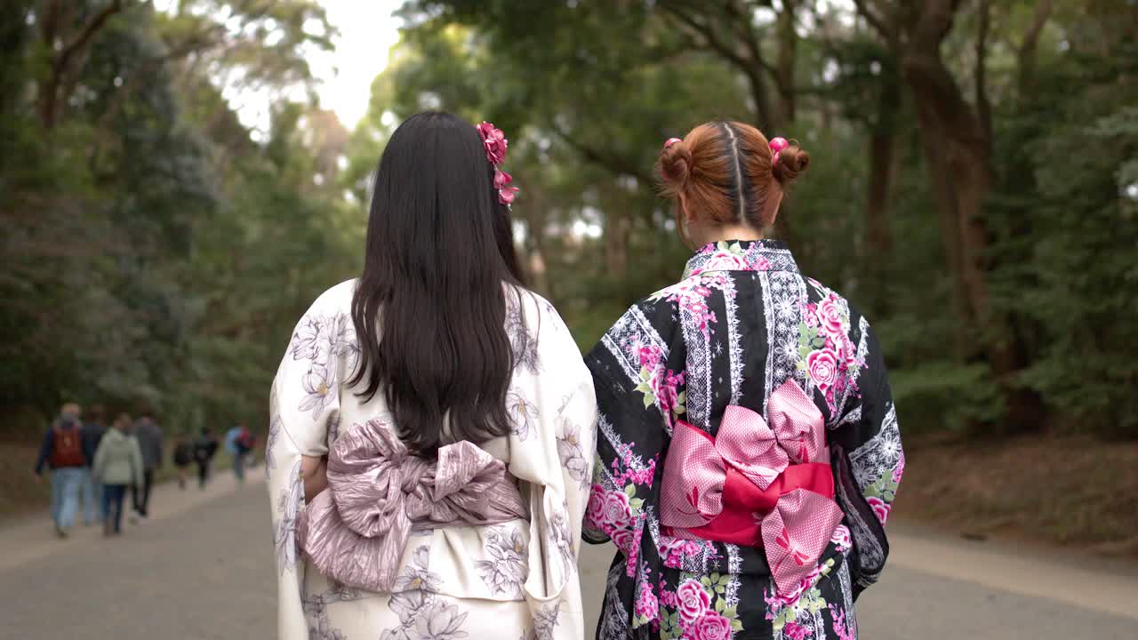 Çiçekli kimonolar giymiş iki kadının bir Japon tapınağı girişinde saygıyla eğilirken arkadan görünümü