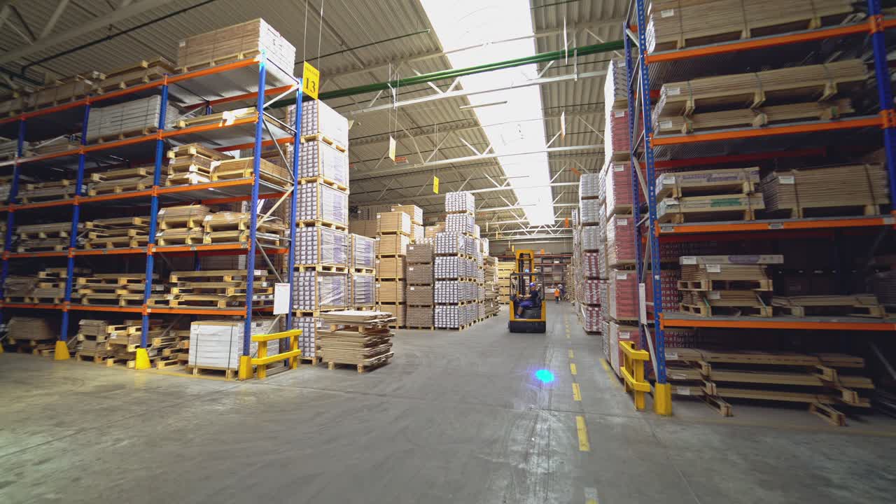 An orange electric stacker is driving between the shelves with goods in stock. Workflow in the company.