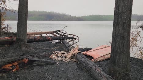 Acercándose-A-La-Orilla-Del-Lago-Con-Algunos-árboles-Desmoronados-En-El-Suelo-Hasta-Una-Canoa-De-Fibra-De-Vidrio-Naranja-Destrozada