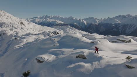 aerial shot in switzerland with a person walking with snow shoes on a sunny day with a glacier behind