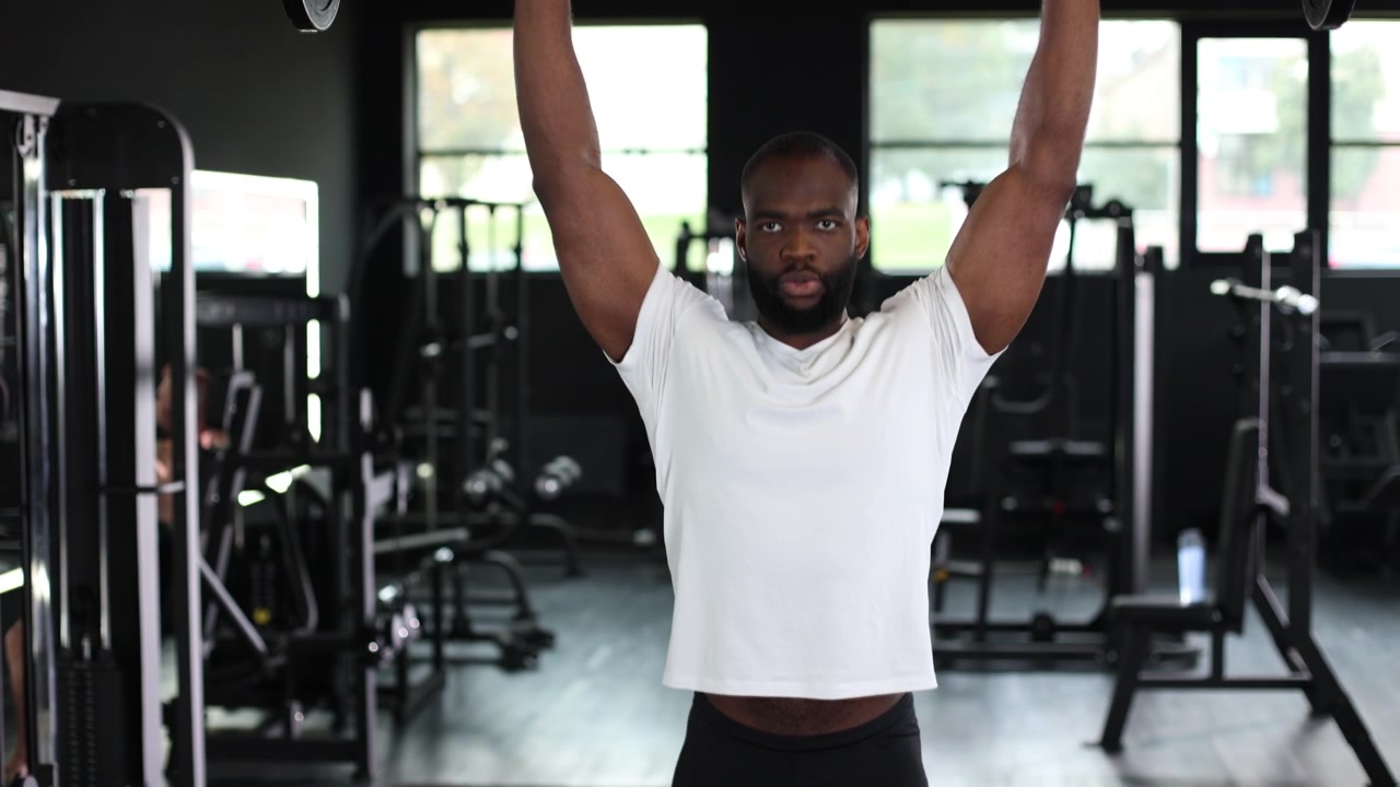 Strong Black Man Performing Barbell Overhead Press in Gym
