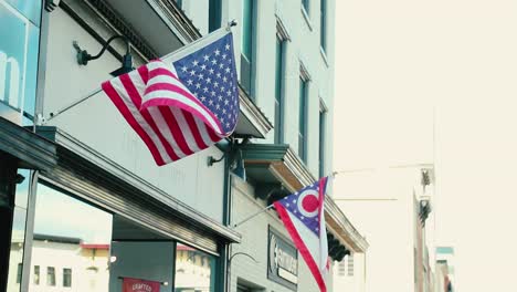 las gloriosas banderas americanas de ohio y nosotros ondean en el bresze frente a una pequeña empresa sobre la acera en una pequeña y pintoresca ciudad
