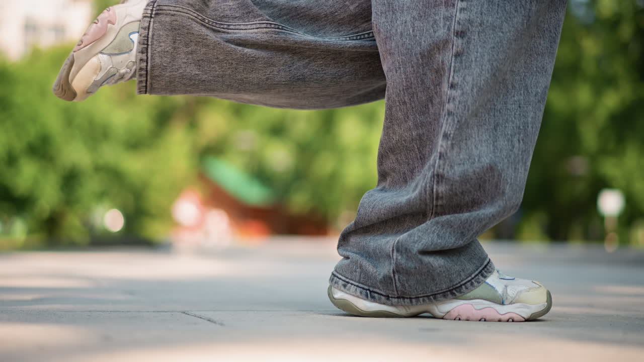 closeup sneakers on sunlit pavement showing relaxed stroll in treelined park, feet and soles in motion, gray sweatpants, rhythmic footsteps, shallow depth of field, warm summer light, routine